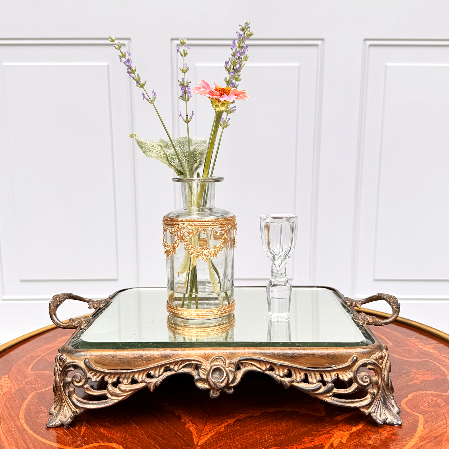 Antique ormolu-mounted blown glass vessel with crystal stopper stood up beside it and fresh flowers displayed inside, front further-back view on mirrored footed tray