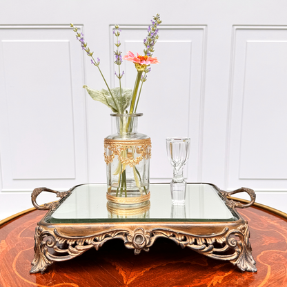 Antique ormolu-mounted blown glass vessel with crystal stopper stood up beside it and fresh flowers displayed inside, front further-back view on mirrored footed tray
