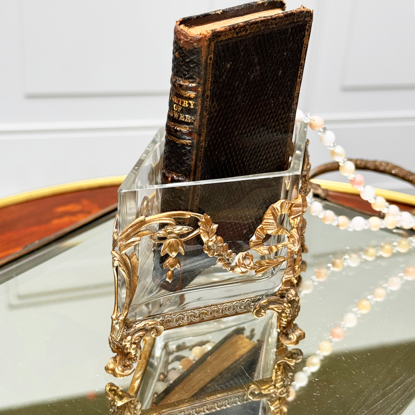 Antique brass-mounted jardinière shown from the side, with a small black leather book inside, placed upon a mirrored surface