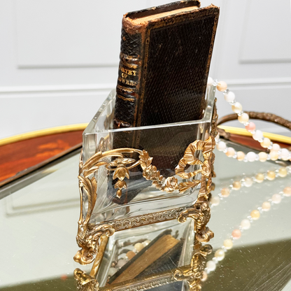 Antique brass-mounted jardinière shown from the side, with a small black leather book inside, placed upon a mirrored surface