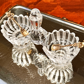 Antique Baccarat double salt cellar with two mini salt spoons, overhead angled view, on mirrored surface