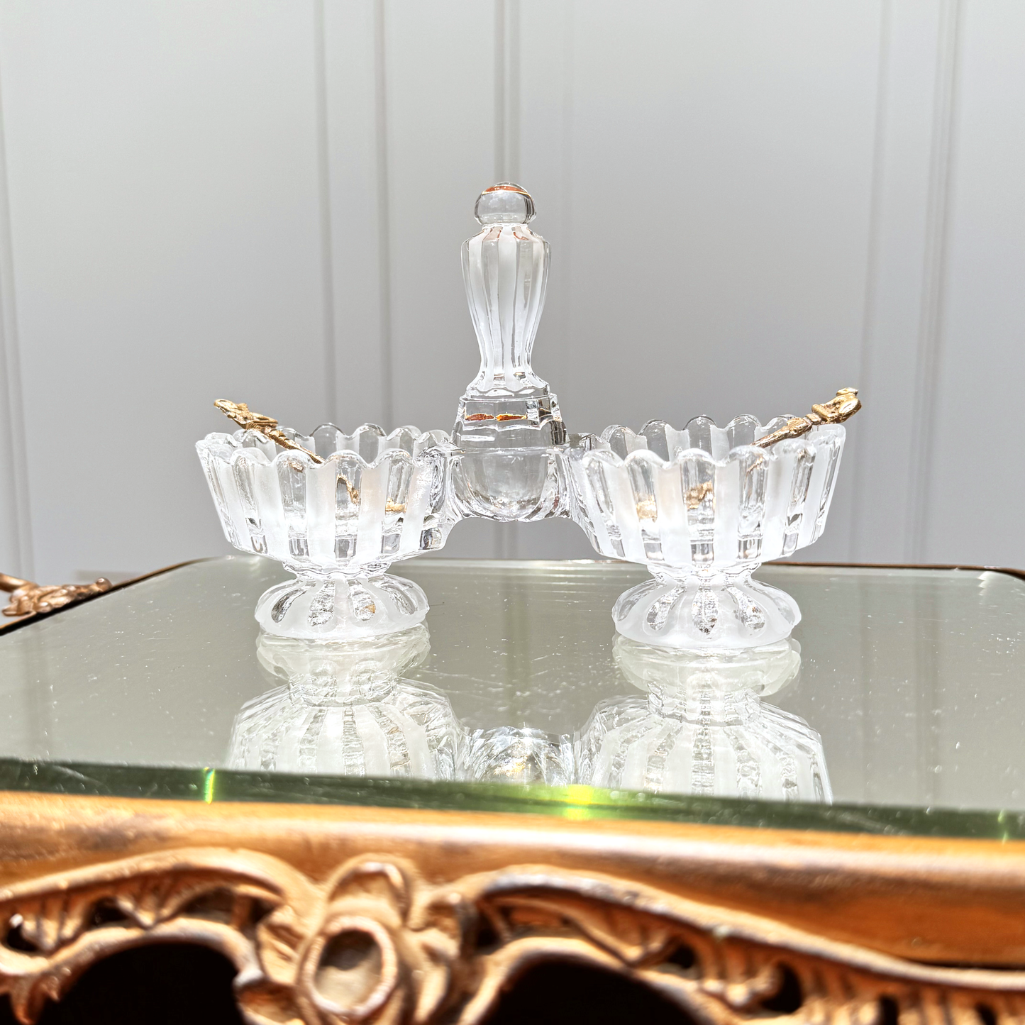 Antique Baccarat crystal double salt cellar with alternating frosted and unfrosted design, front view on mirrored surface, with two small gold colored spoons, one in each side