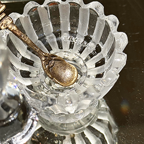 Close-up of the Baccarat maker's mark on the inside of the crystal salt cellar, mini spoon also inside salt cellar, on mirrored surface