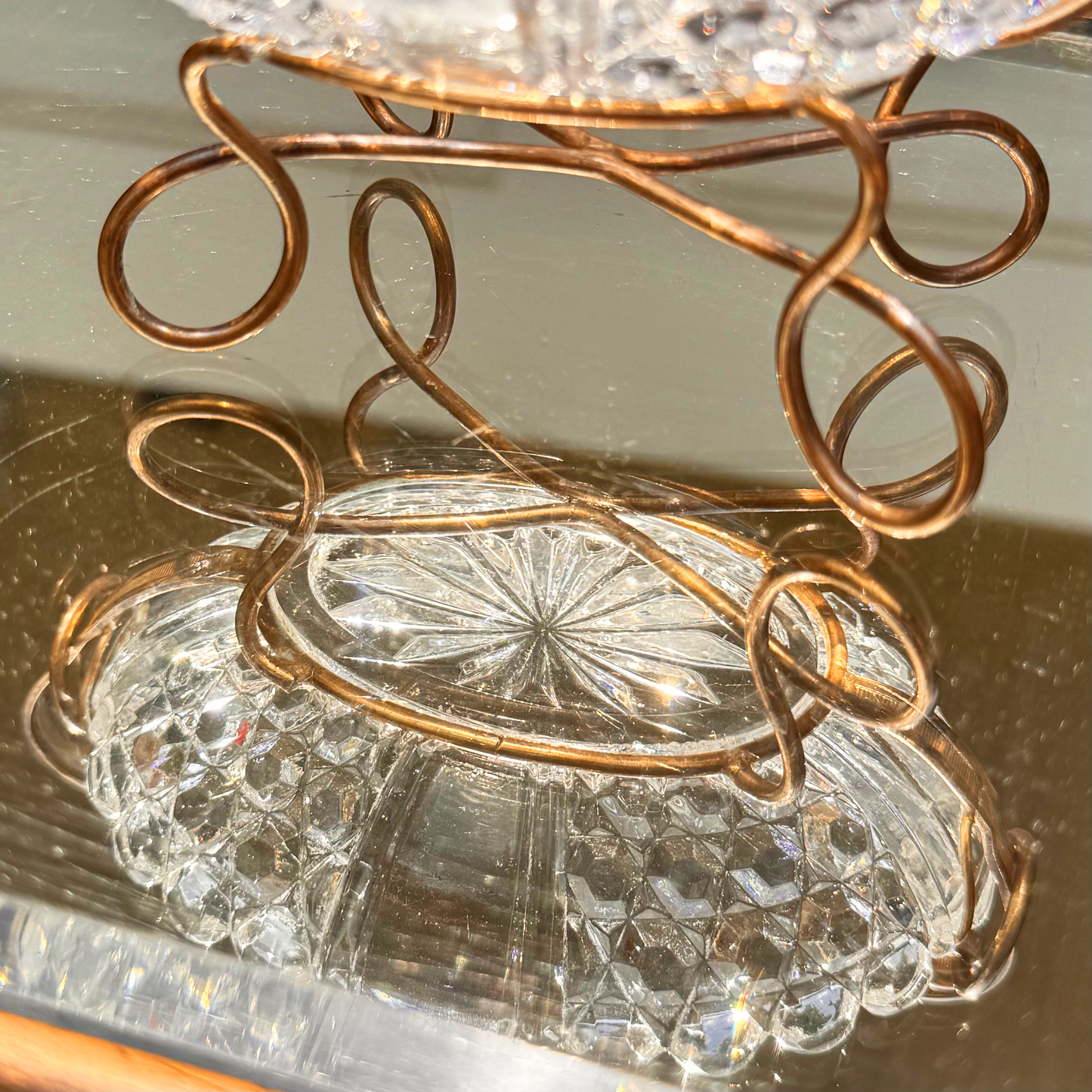 Antique Baccarat crystal catchall close up on the spiral brass wired mounting reflecting also the crystal bowl in the mirror surface it's placed on