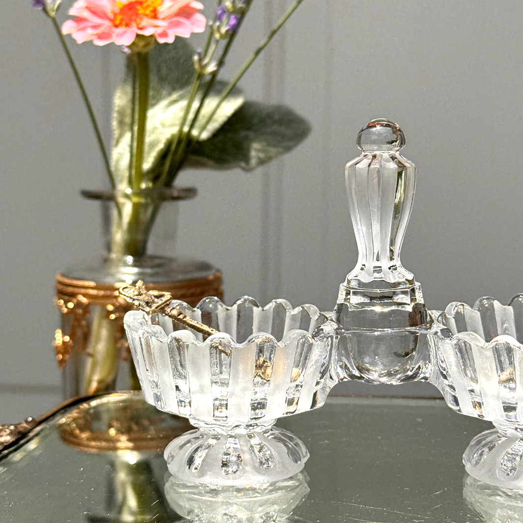 Antique Baccarat double salt cellar with two mini salt spoons, close-up view of left side, on mirrored surface