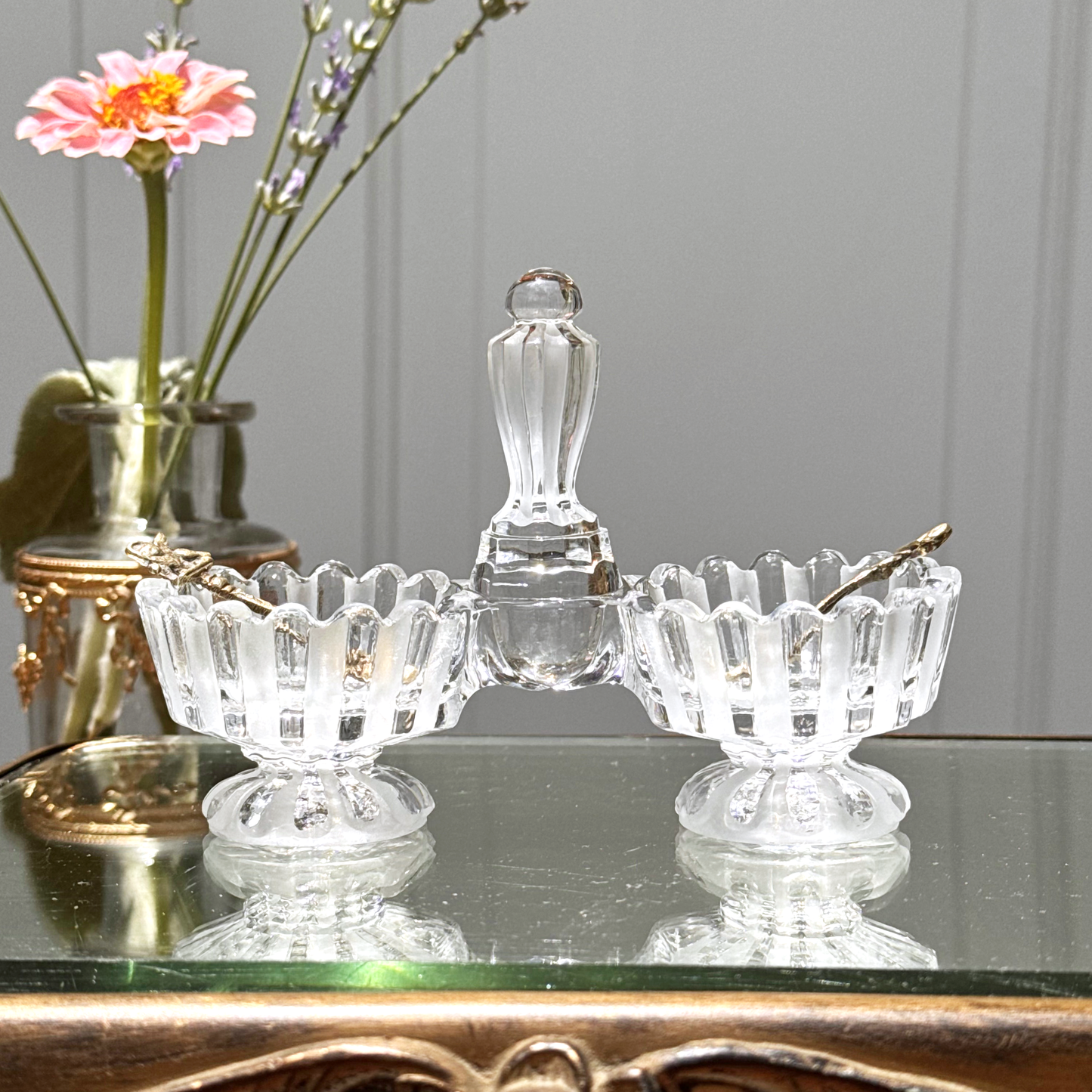 Antique Baccarat crystal double salt cellar close-up with alternating frosted and unfrosted design, front view on mirrored surface, with two small gold colored spoons, one in each side