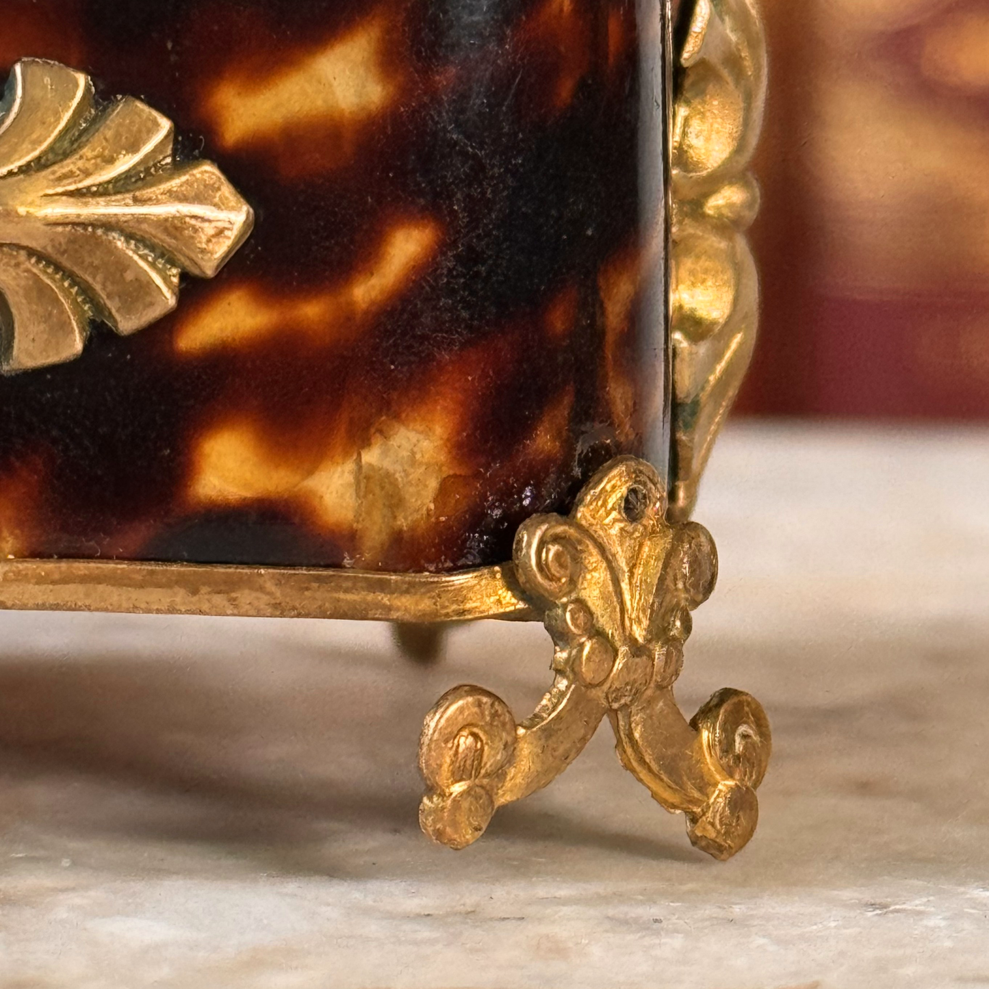 An antique miniature footed tortoiseshell jewelry casket with brass mounts and a beveled glass top, resting on a marble surface, shown close-up of foot not sitting evenly on marble