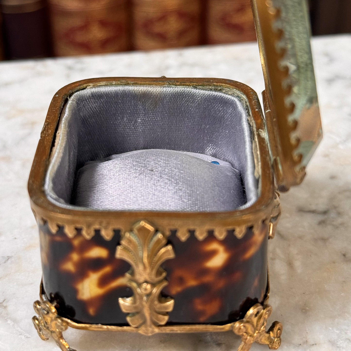 An antique miniature footed tortoiseshell jewelry casket with brass mounts and a beveled glass top, resting on a marble surface, shown open from side highlighting interior