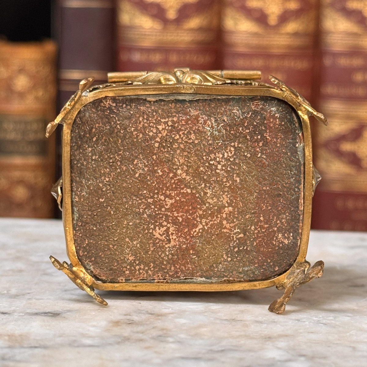 An antique miniature footed tortoiseshell jewelry casket with brass mounts and a beveled glass top, resting on a marble surface, shown from bottom with textured leather bottom lining