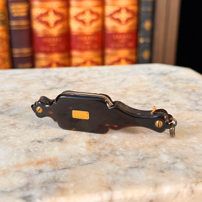An antique folding lorgnette and spectacles shown folded with a tortoiseshell handle, gold plaque, and silver metal frames, resting on a marble surface