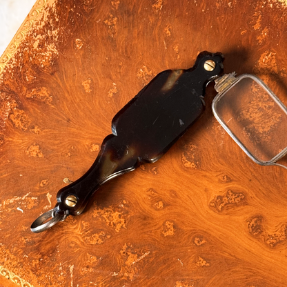 An antique folding lorgnette and spectacles shown unfolded with a tortoiseshell handle, silver colored frames,  resting on a leather book, close-up of backside of handle