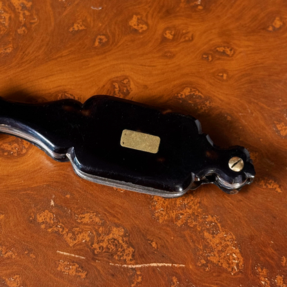 An antique folding lorgnette and spectacles shown folded with a tortoiseshell handle, gold plaque, and silver colored frames, resting on a leather book, close up on plaque and top front