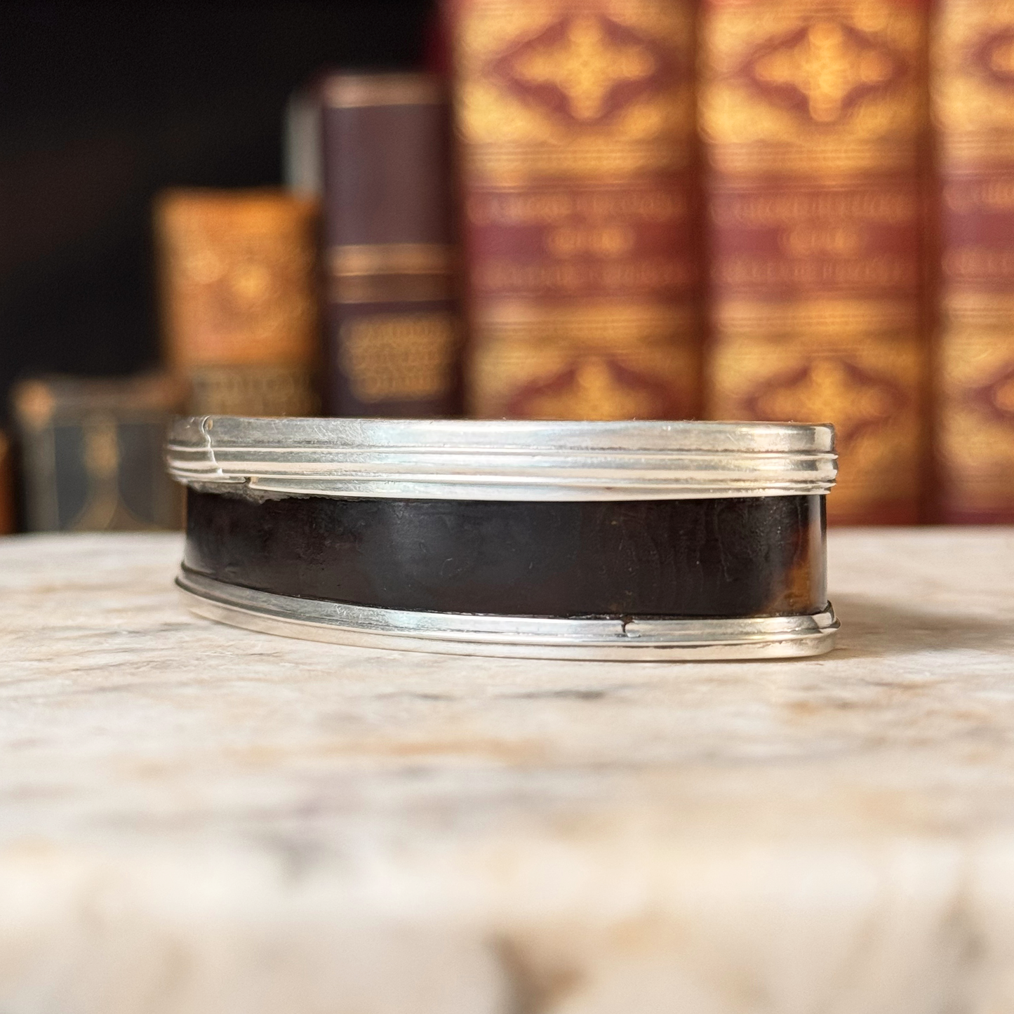 An antique oval tortoiseshell, mother-of-pearl, and silver snuff box, shown from the side highlight the tortoiseshell and silver mounting