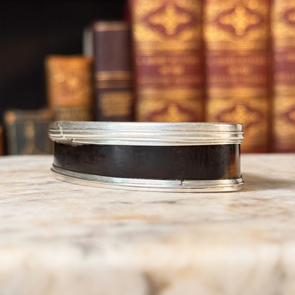 An antique oval tortoiseshell, mother-of-pearl, and silver snuff box, shown from the side highlight the tortoiseshell and silver mounting