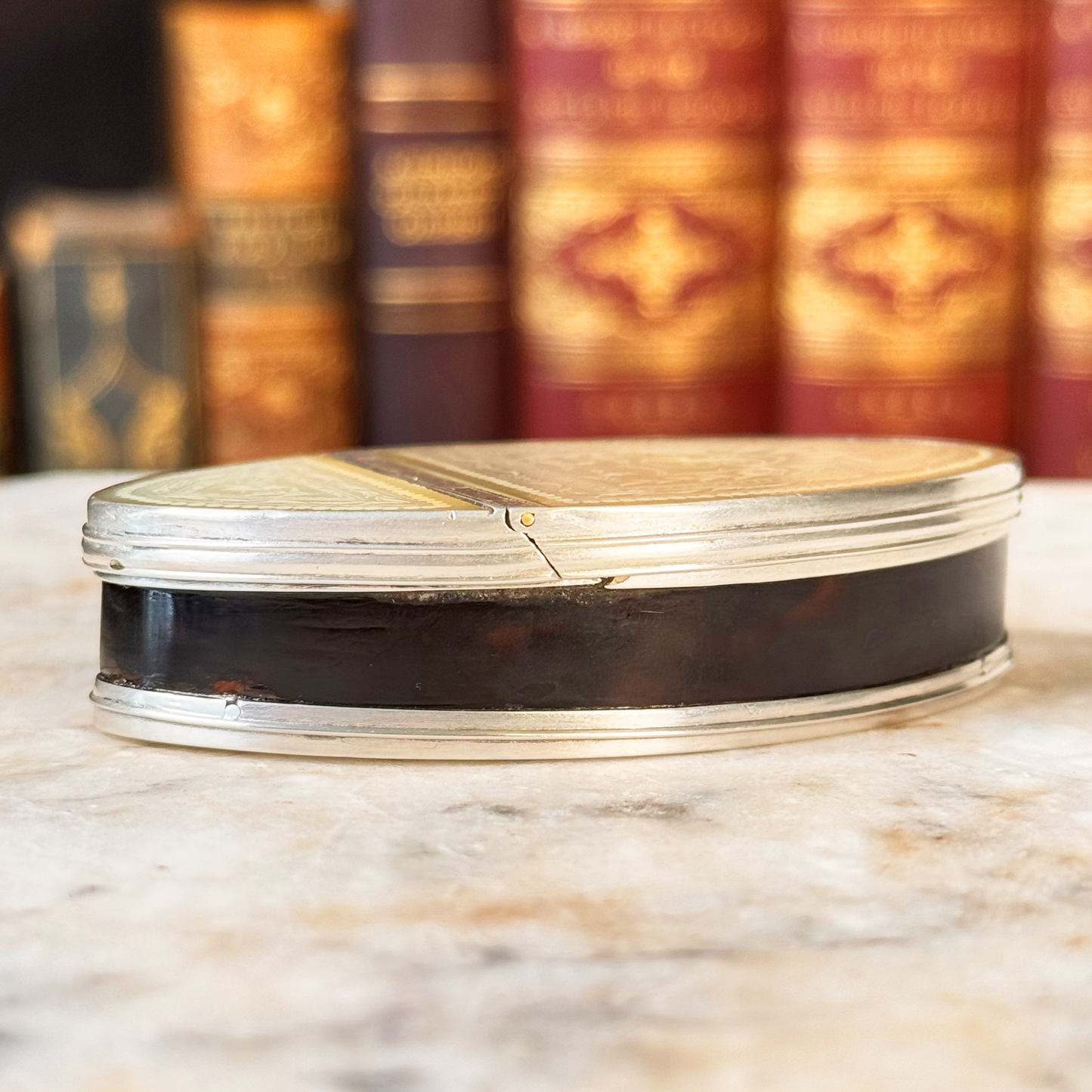 An antique oval tortoiseshell, mother-of-pearl, and silver snuff box, shown from the front highlight the tortoiseshell and silver mounting
