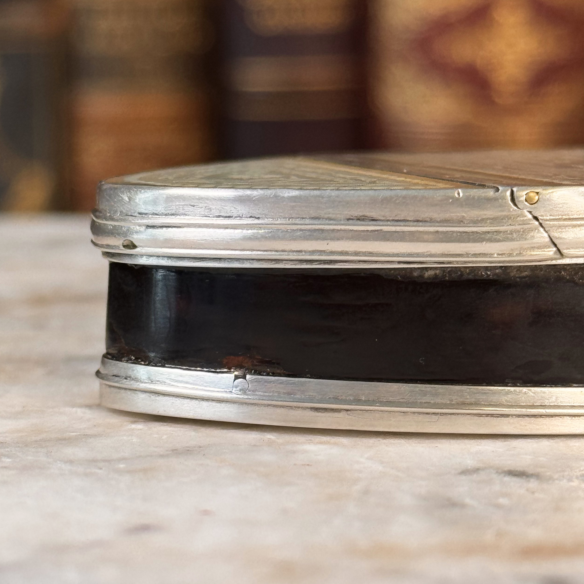 An antique oval tortoiseshell, mother-of-pearl, and silver snuff box, shown close-up to highlight the silver mounting