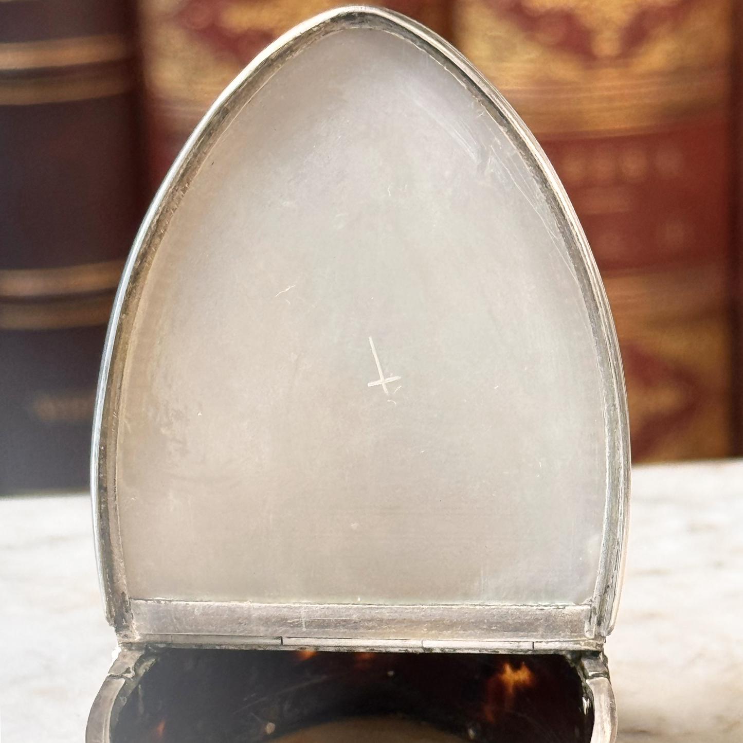 An antique oval tortoiseshell, mother-of-pearl, and silver snuff box, shown open highlighting the etched cross on the mother-of-pearl lid
