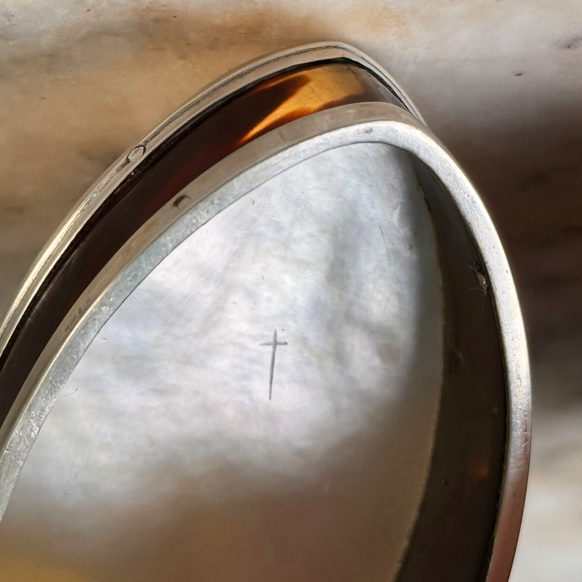 An antique oval tortoiseshell, mother-of-pearl, and silver snuff box, shown open highlighting the etched cross on the inside base of the mother-of-pearl bottom
