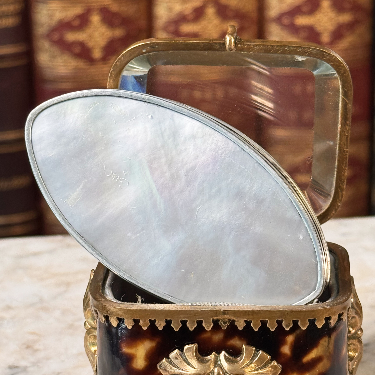 An antique oval tortoiseshell, mother-of-pearl, and silver snuff box, placed in a miniature jewelry box, close up of mother-of-pearl bottom