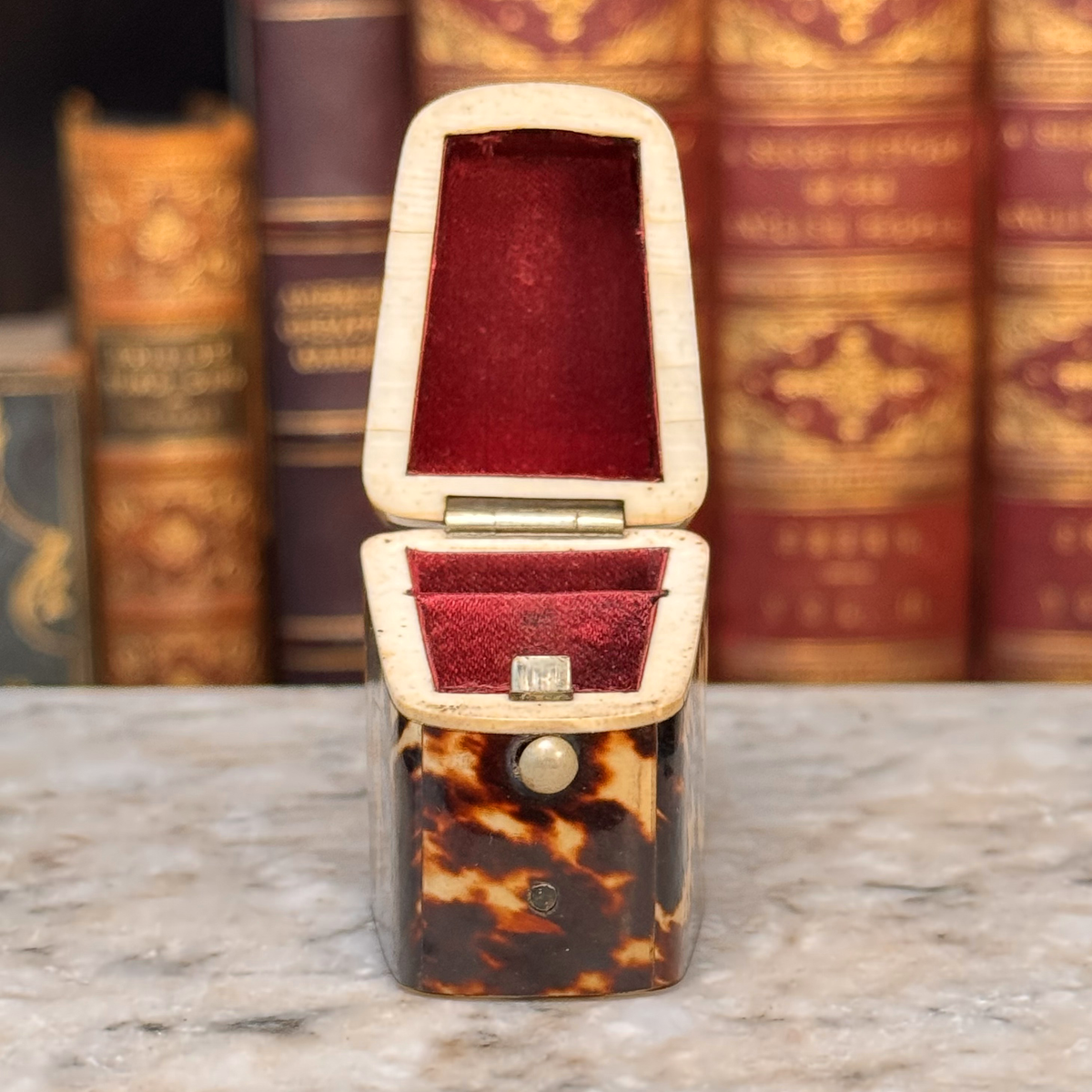 An antique tortoiseshell box with a glossy dark brown and amber pattern, a small round button, shown open with red silk lining on top and bottom