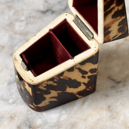 An antique tortoiseshell box with a glossy dark brown and amber pattern, a small round button, shown open with red silk lining on top and bottom, viewed from above