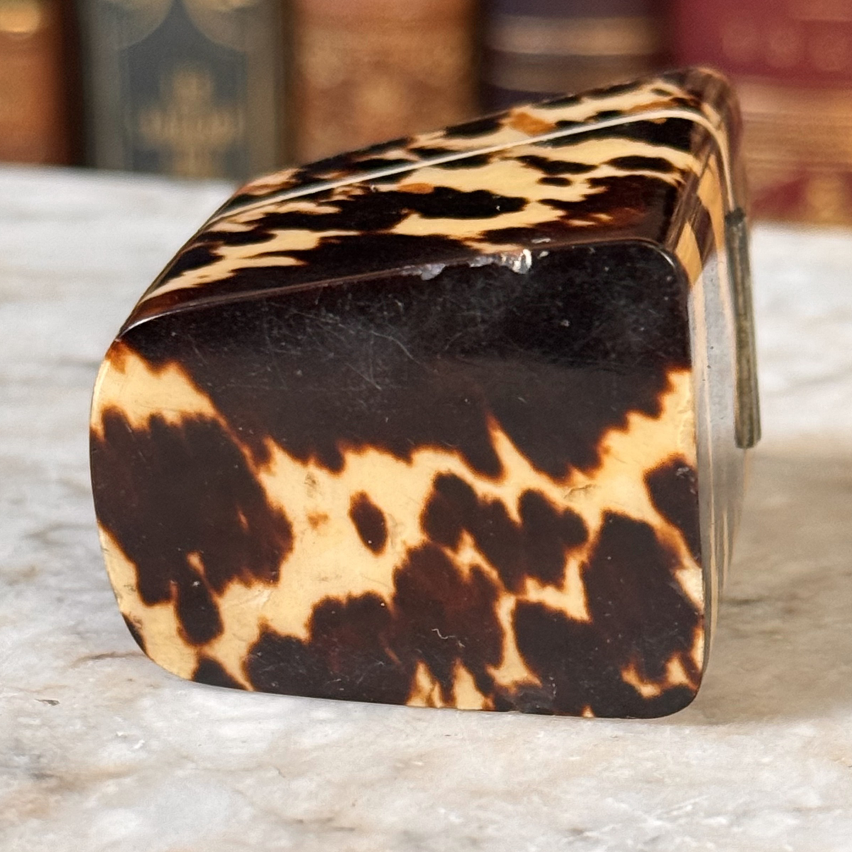 An antique tortoiseshell box with a glossy dark brown and amber pattern, shown from the bottom featuring some chipping to one edge
