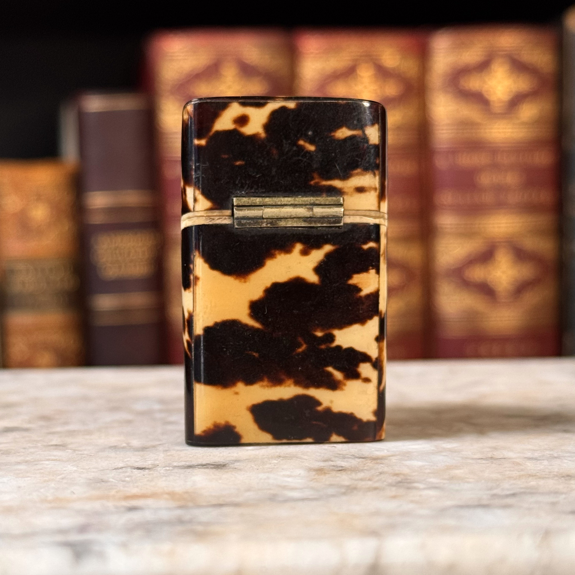 An antique tortoiseshell box with a glossy dark brown and amber pattern, shown closed from the backside featuring the hinge