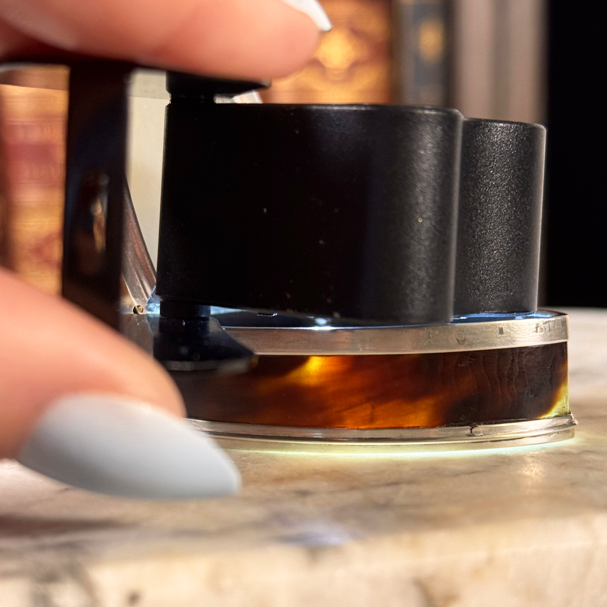 An antique oval tortoiseshell, mother-of-pearl, and silver snuff box, with a lighted loupe shining inside to highlight the tortoiseshell