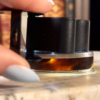 An antique oval tortoiseshell, mother-of-pearl, and silver snuff box, with a lighted loupe shining inside to highlight the tortoiseshell