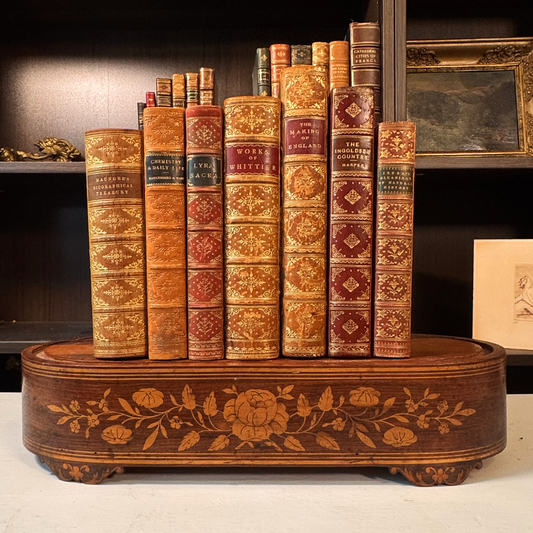 Antique wood marquetry riser with floral inlay, books displayed on top, bookshelf background