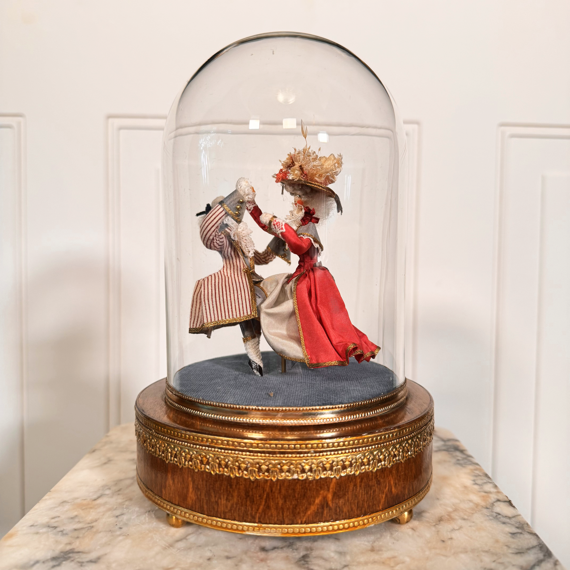 Diorama of two people in formal attire under a glass dome on a marble surface.
