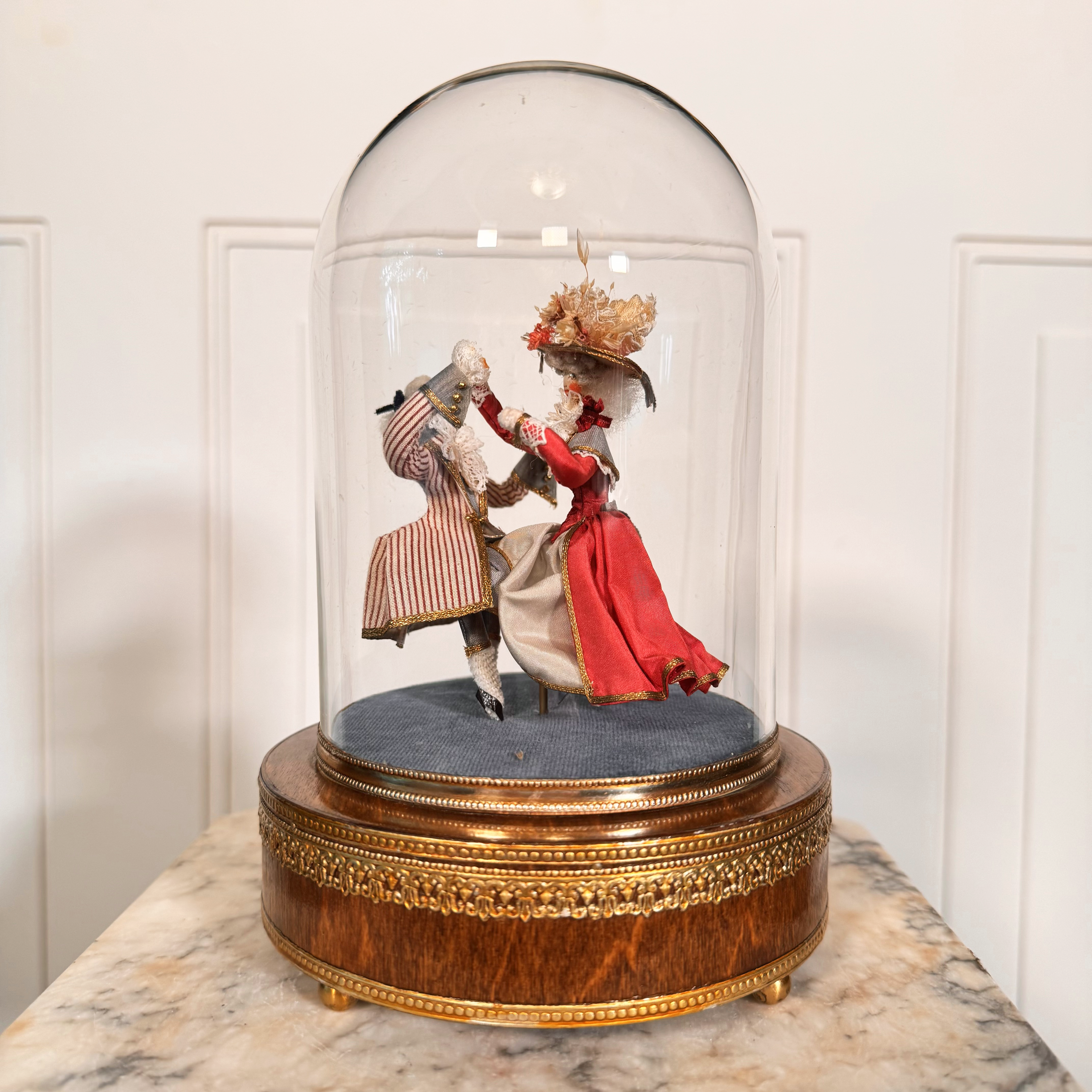 Diorama of two people in formal attire under a glass dome on a marble surface.