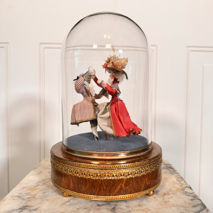 Diorama of two people in formal attire under a glass dome on a marble surface.
